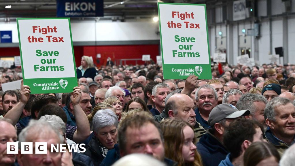 A sea of faces at the Eikon Exhibition Centre in Lisburn. Two signs are being held aloft, both saying - Fight the Tax, Save our Farms.
