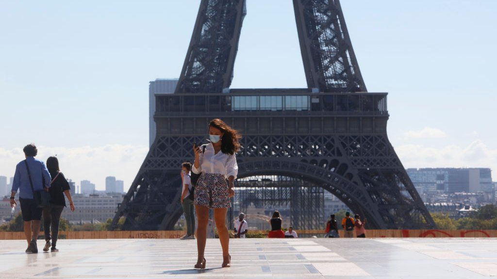 A woman in a face mask walks in front of the Eiffel Tower in Paris