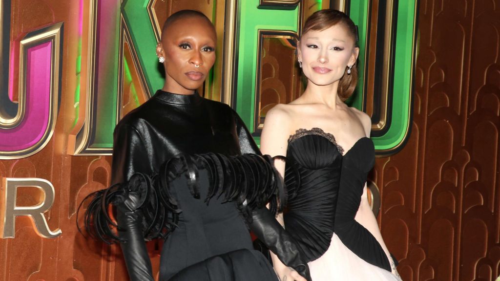 Cynthia Erivo in a black top with leather or leather-look sleeves and feathers and Ariana Grande in a corset-style strapless dress which is black at the top with a taffeta white skirt. They are at the New York premiere of Wicked: For Good.