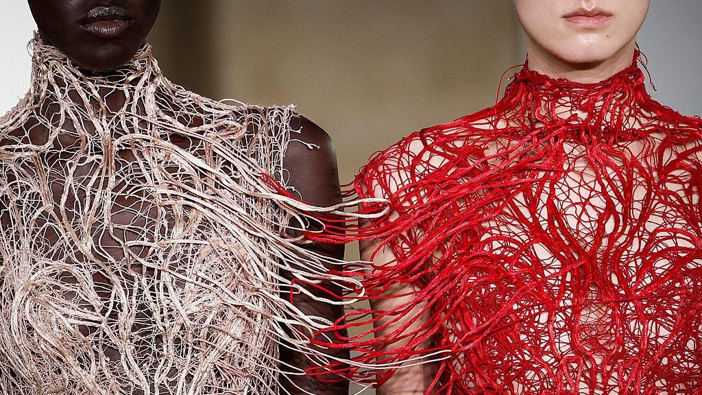 Two models - the bottom of their faces and torsos visible - wear elaborate outfits made of white and red looped material