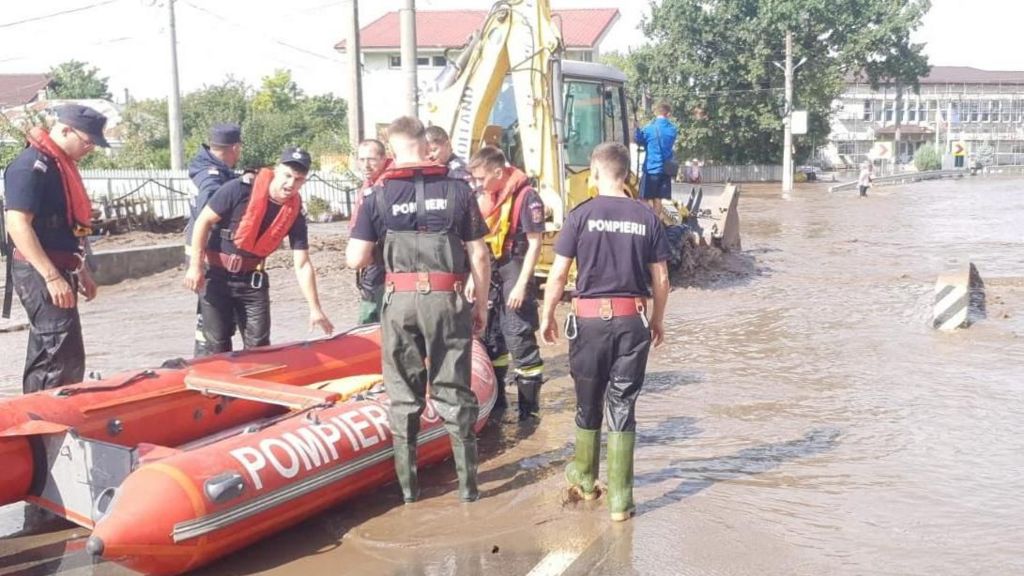 Firefighters move an inflatable red rescue boat into position on a flooded road in Romania.