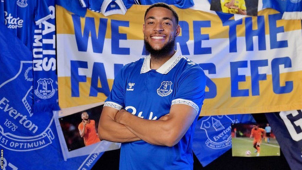 Arnaut Danjuma in an Everton shirt in front of Everton banners and posters