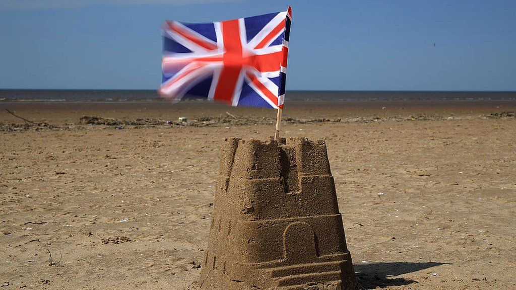 Union Jack flag sits on top of a sand castle on a beach