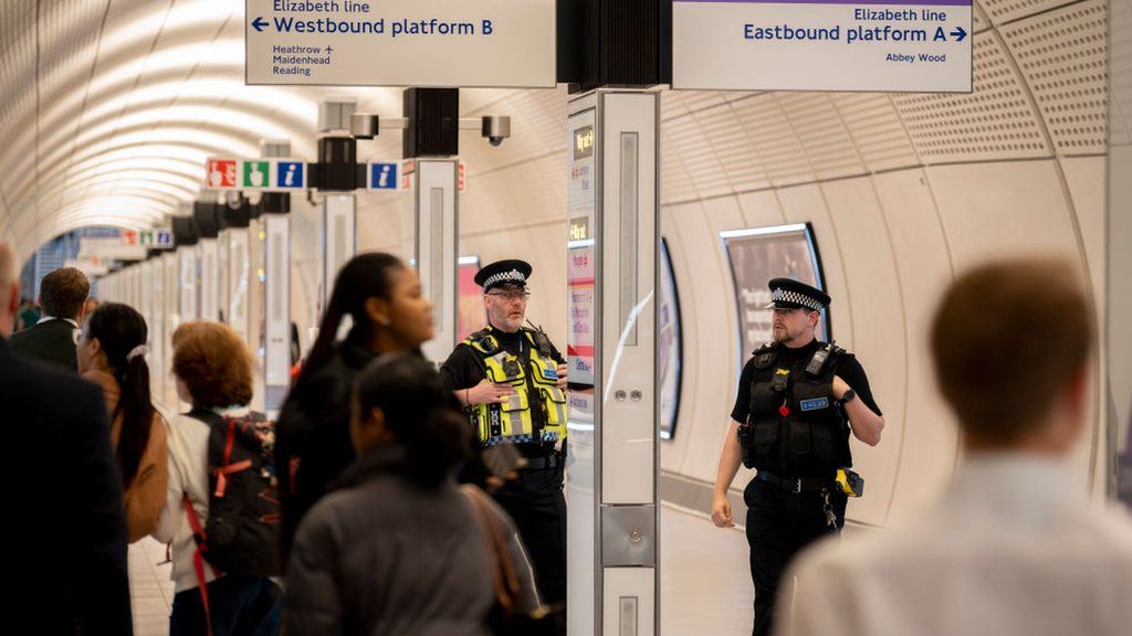 Two police officers standing an in Elizabeth line station as commuters pass