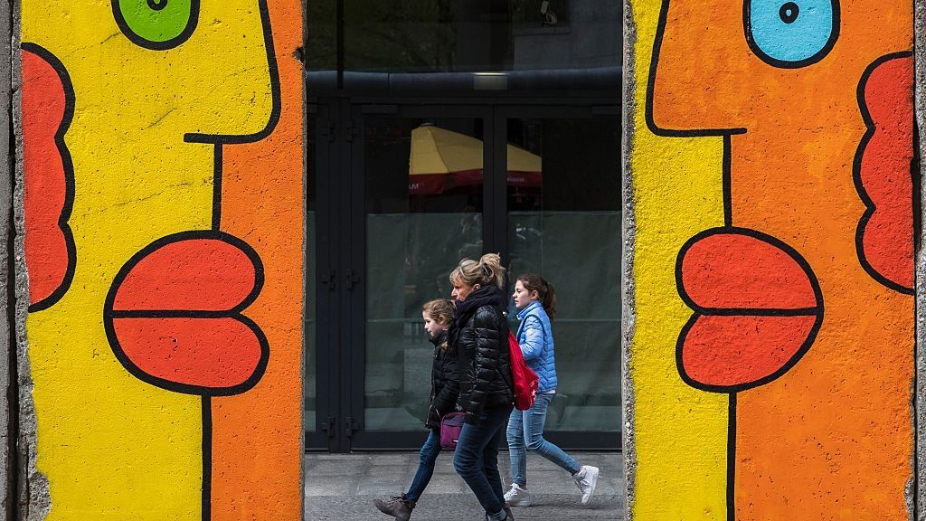 Shoppers are seen between the gap of remnants of the Berlin wall at Potsdamer Platz in Berlin on April 27, 2016