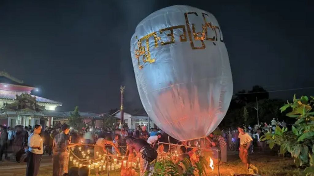 People lighting candles in the night time around a giant white balloon