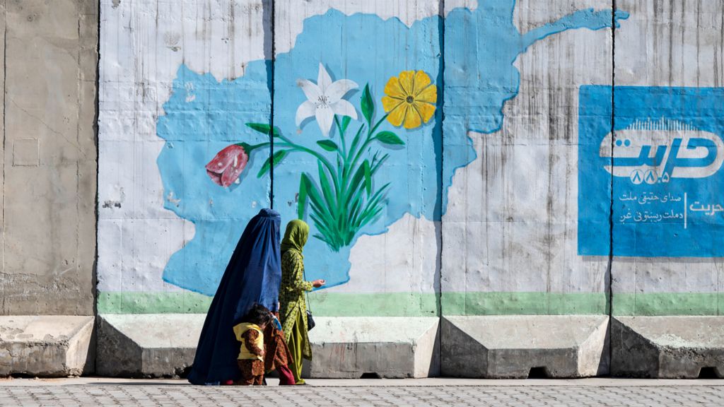 An Afghan burqa-clad woman walks past a wall mural with the map of Afghanistan, in Kabul on February 1, 2024. (Photo by Wakil KOHSAR / AFP) (Photo by WAKIL KOHSAR/AFP via Getty Images)