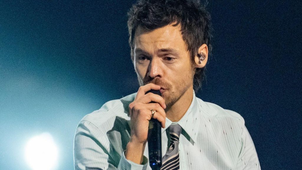 Harry Styles in a blue/grey shirt and tie, singing into a microphone on stage at the Brit Awards 2026.