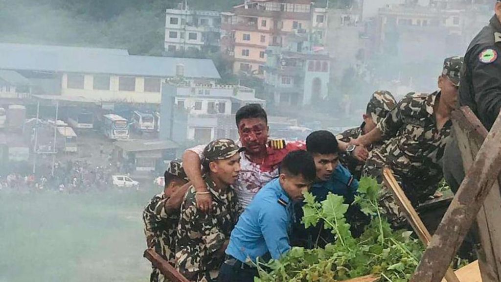 The pilot of the crashed plane emerges from the wreckage with blood on his face