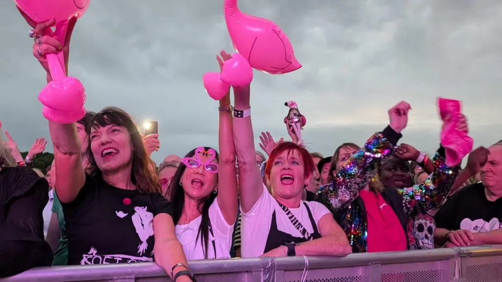 Festival-goers bathed in purple light and waving inflatable flamingos listen to Marc Almond performing at the Godiva Festival in 2025.