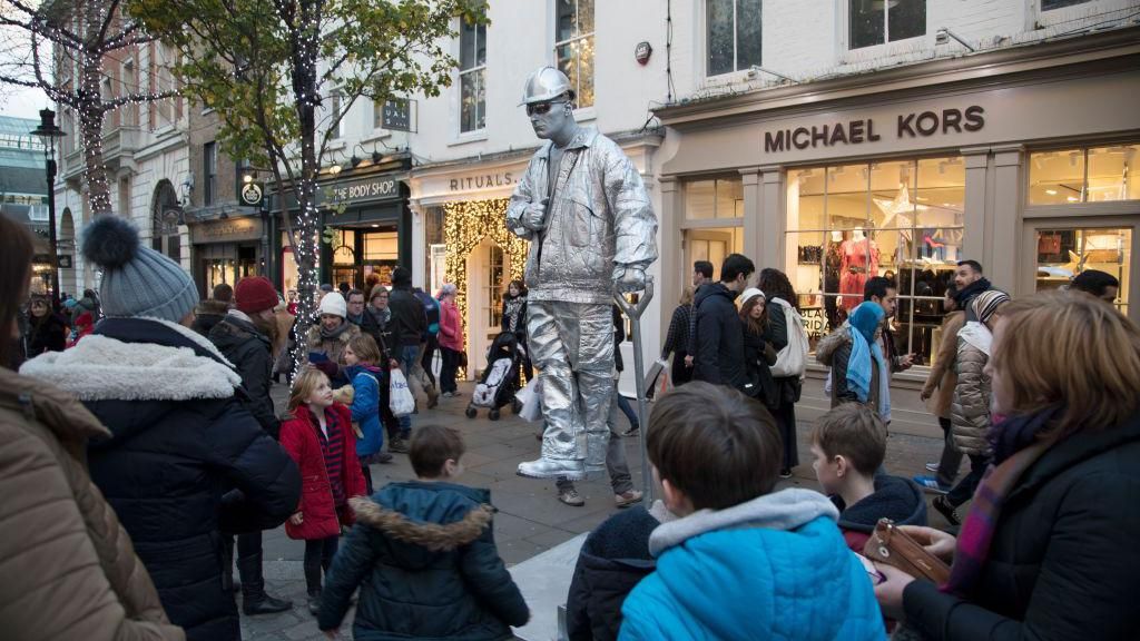 Silver painted living statue street performer sits totally still as if floating in mid air, and delighting passers by and tourists in Covent Garden, London
