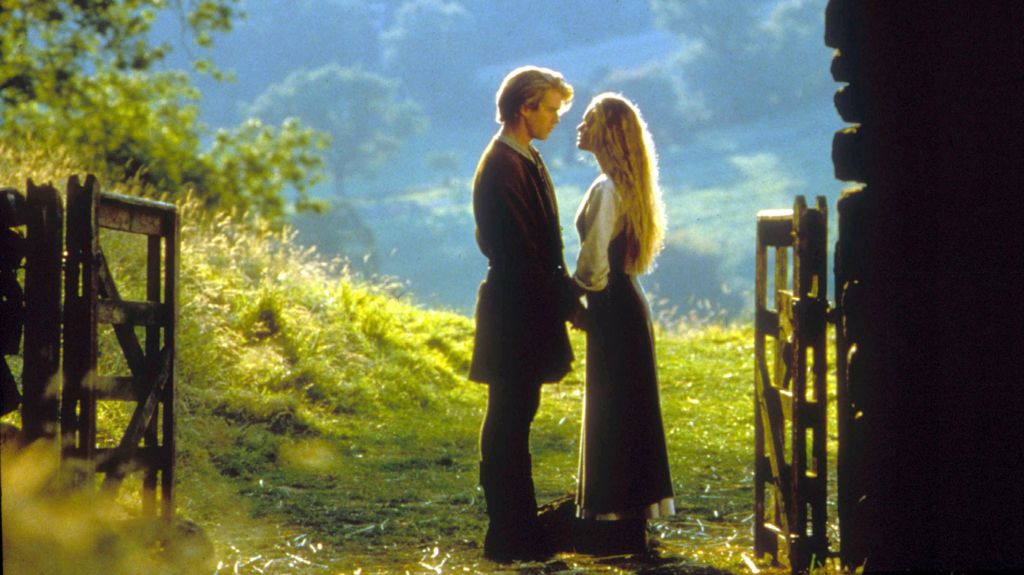 Cary Elwes and Robin Wright standing facing each other and holding hands in a sunlit field in a scene from The Princess Bride