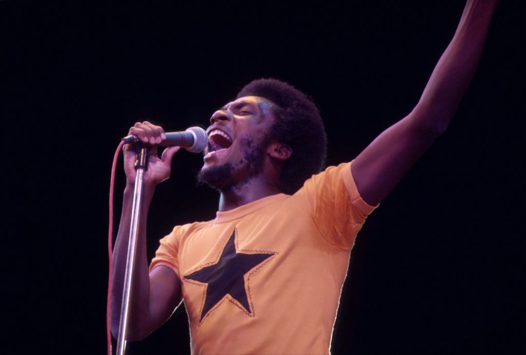 Jimmy Cliff performing on stage, wearing an orange T-shirt with a black star on it