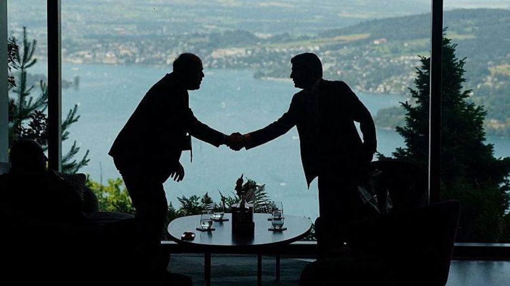 Two figures in silhouette shake hands with a lake visible behind them, at talks in Switzerland between the US and Iran