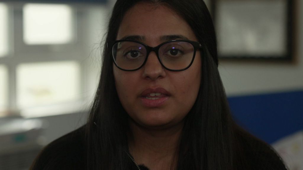 Jaspreet wears dark rimmed glasses and a black top, she has shoulder length dark hair.