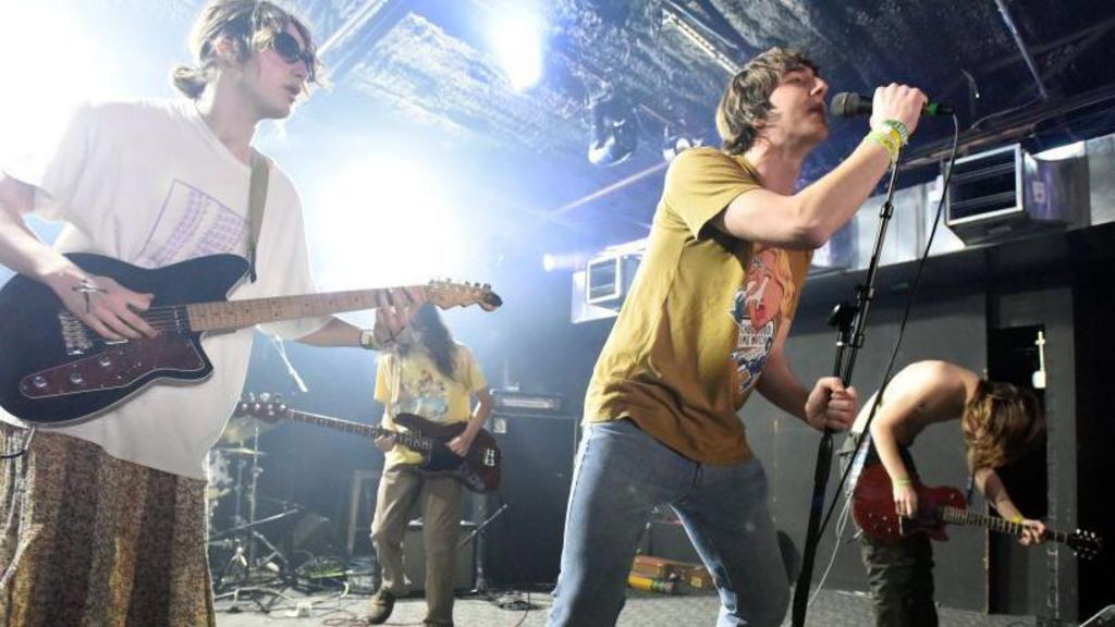 All four members of Geese performing live on stage with their guitars