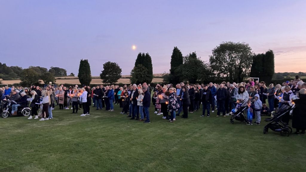 Crowds with candles gather on a field at night