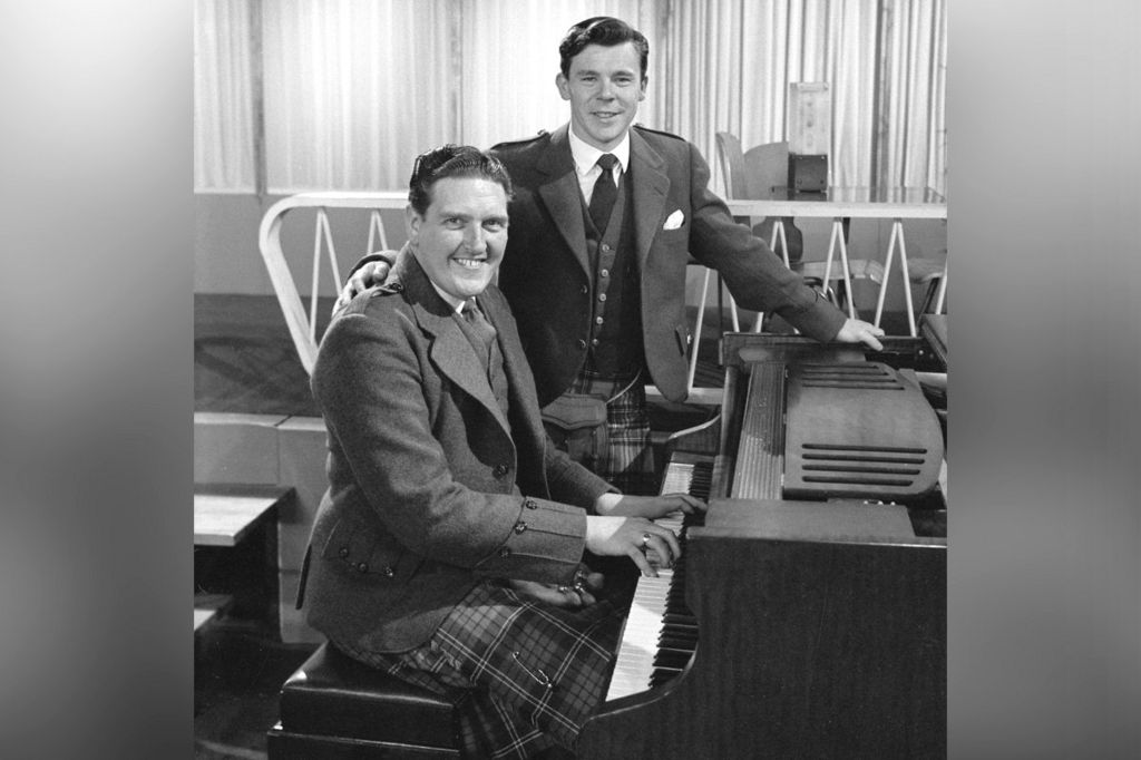 Singer and musician Alistair McHarg with Andy Stewart (standing), host of programme The White Heather Club.