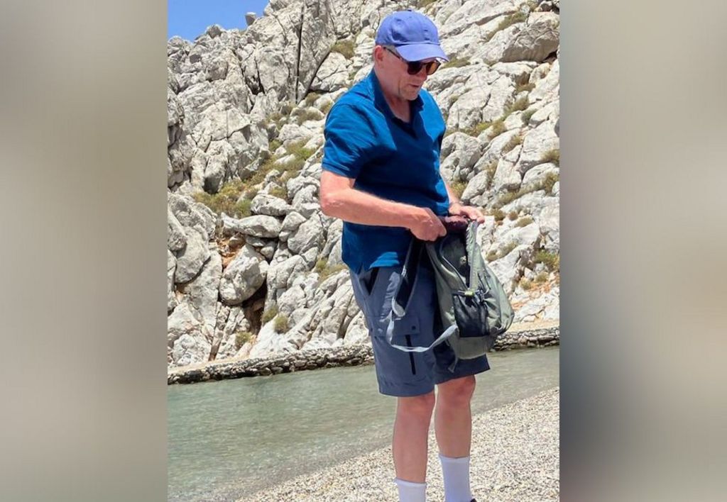 Michael Mosley on a beach, he is wearing a blue cap, sunglasses and a blue Polo shirt