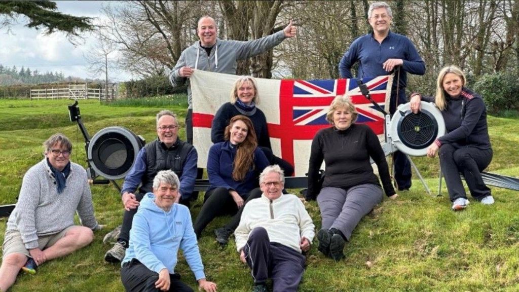 10 people posing on a lawn near rowing machines and with two people holding up a union jack/England flag