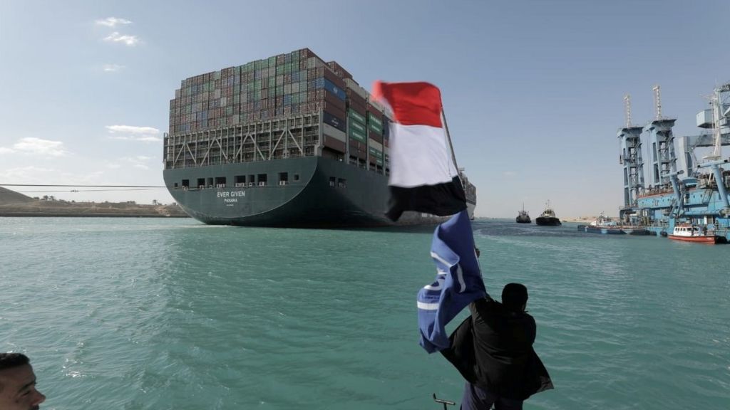A man waves an Egyptian flag after the Ever Given is fully refloated in the Suez Canal, Egypt (29 March 2021)