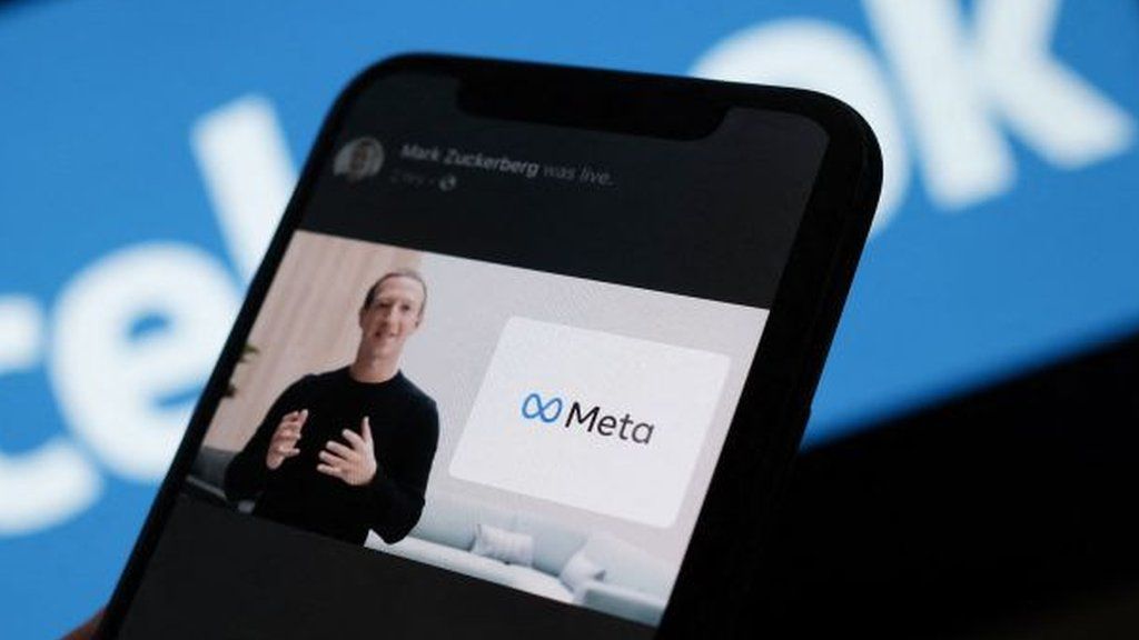 Mark Zuckerberg and meta logo shown on a phone screen with facebook logo in the background in a stock illustration