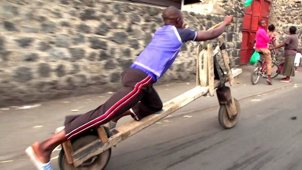 Tumaini riding his chukudu, which looks like a stretched wooden bicycle