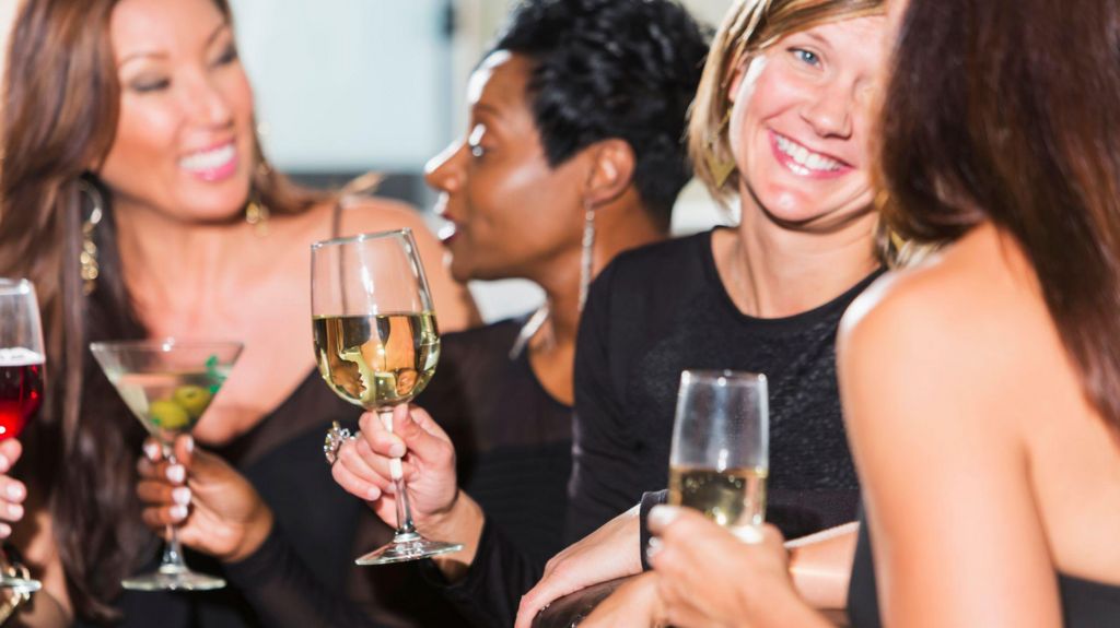 Four women in their thirties chatting with drinks in their hands