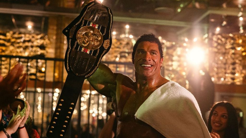 Dwayne Johnson as UFC fighter Mark Kerr in The Smashing Machine, with a towel around his shoulders and surrounded by people applauding