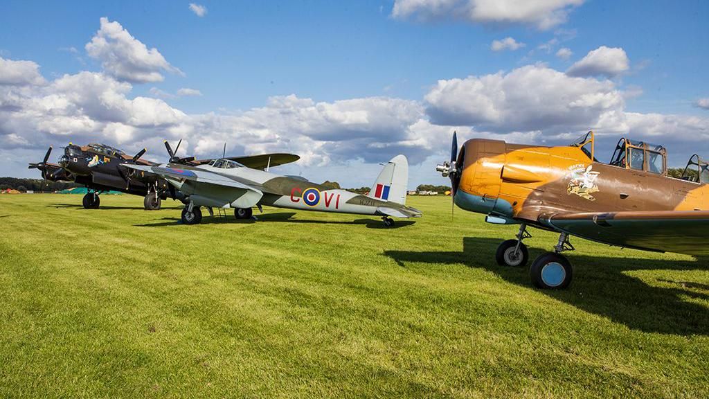 Three vintage planes lined up on a grassy field 