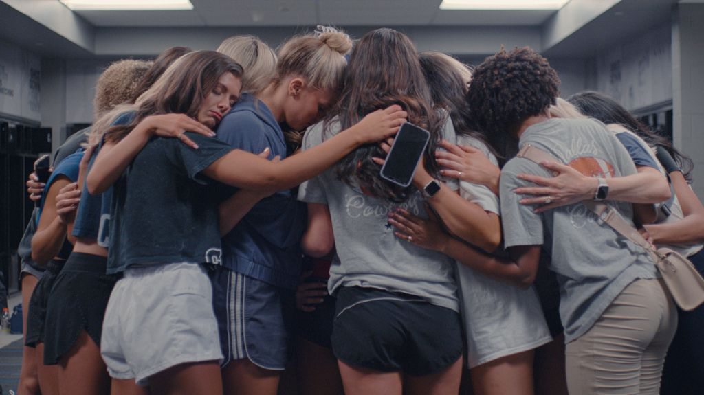 A large group of cheerleaders looking upset and consoling each other in a huddle