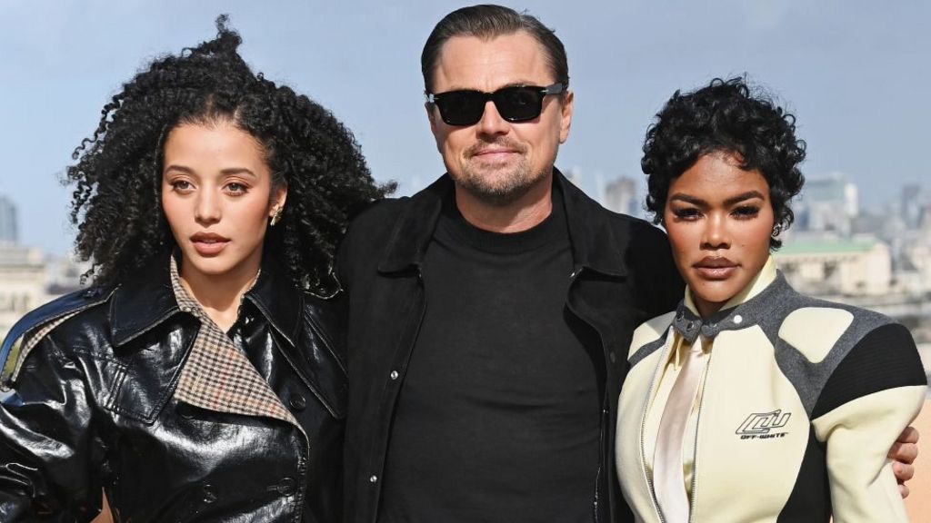 Chase Infiniti, Leonardo DiCaprio and Teyana Taylor attend the London photocall for One Battle After Another in London in September. Infiniti is wearing a black shiny jacket, DiCaprio has a black jacket and T-shirt on and Taylor has on a racing-style cream, grey and black jacket.