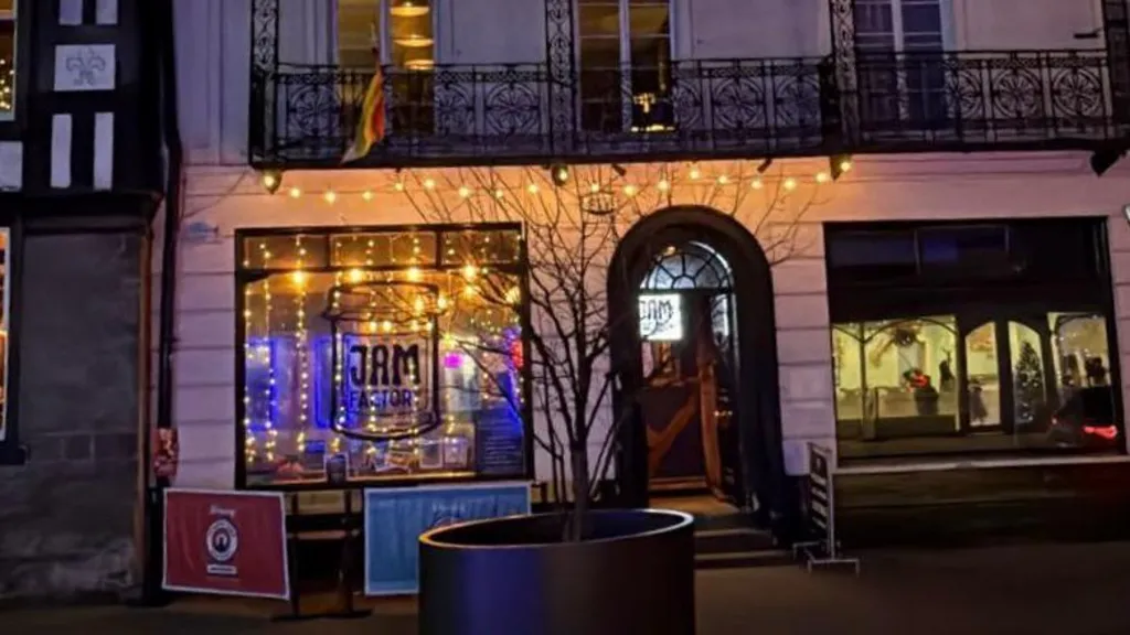 An exterior shot of the Jam Factory venue in Hereford. It is lit with fairy lights and has a red and blue barrier outside the window. There is a Jam Factory logo painted on the window.