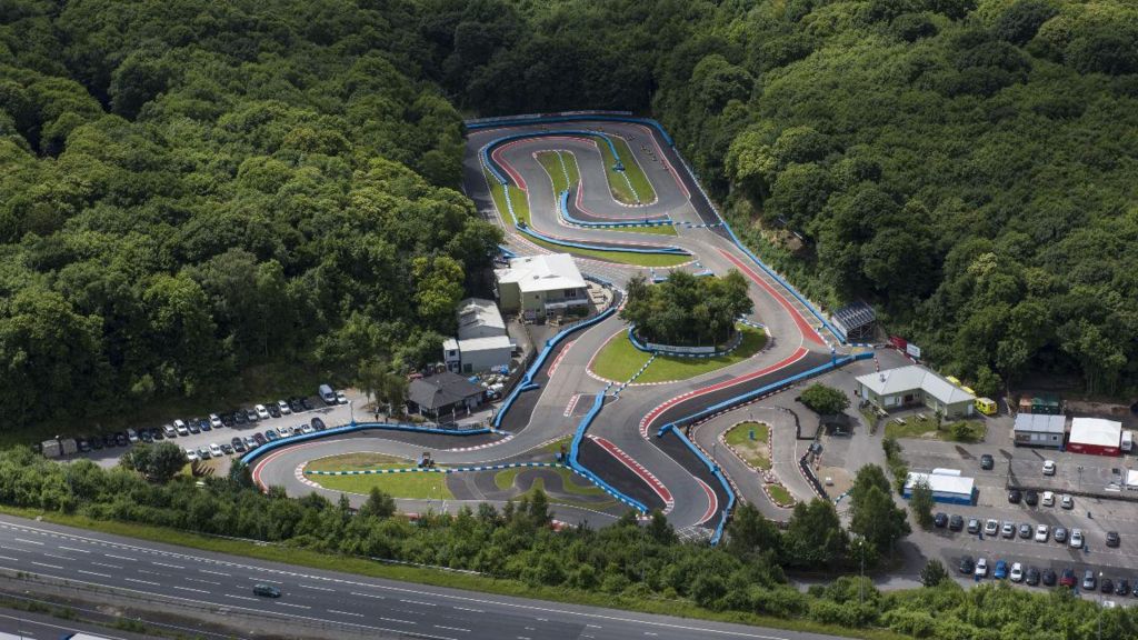 An aerial image of Buckmore Park karting circuit surrounded by lush green trees and with bright red and blue markings visible around the track