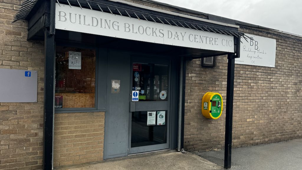 The entrance to a community hub, it has a sign saying Building Blocks Day Centre CIC. There is a defibrillator in a yellow and green case on the wall outside. 