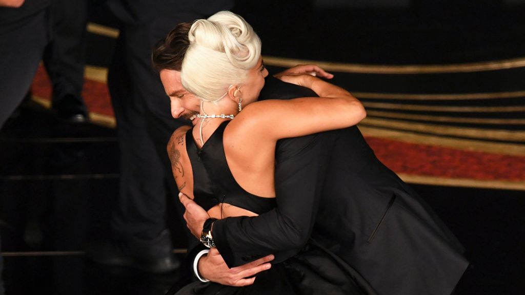 Lady Gaga and Bradley Cooper embracing in smart, black outfits at the Oscars
