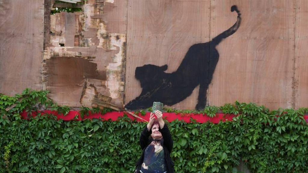 A woman taking a selfie next to the painting 