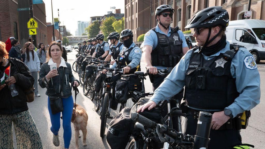 A women walks her dog past police who are keeping activist across the street from campus while workers and police remove a pro-Palestinian encampment at DePaul University in May. 