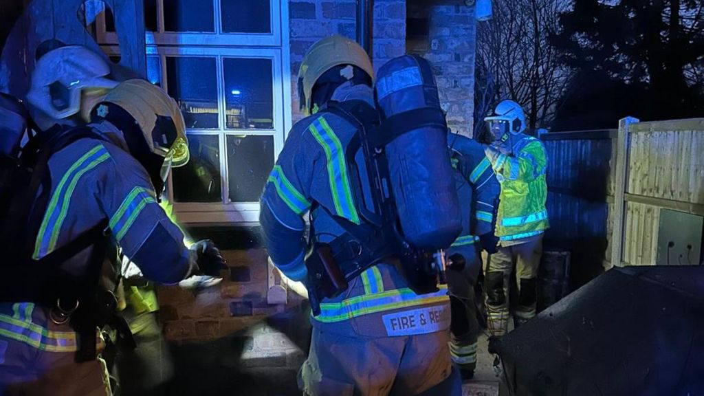 Four firefighters in breathing apparatus outside the house