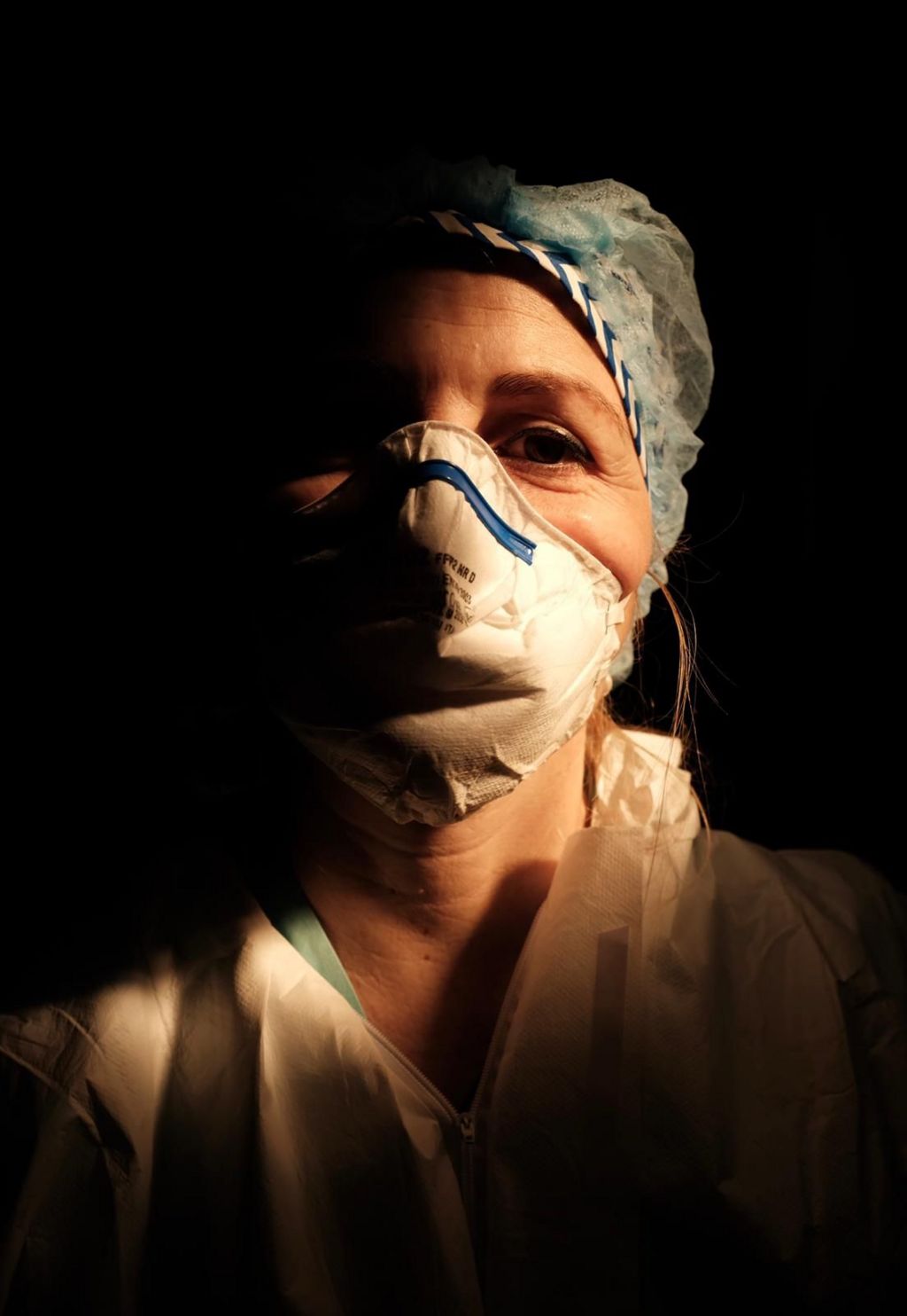 A female nurse wearing a face mask with a dark background behind her.