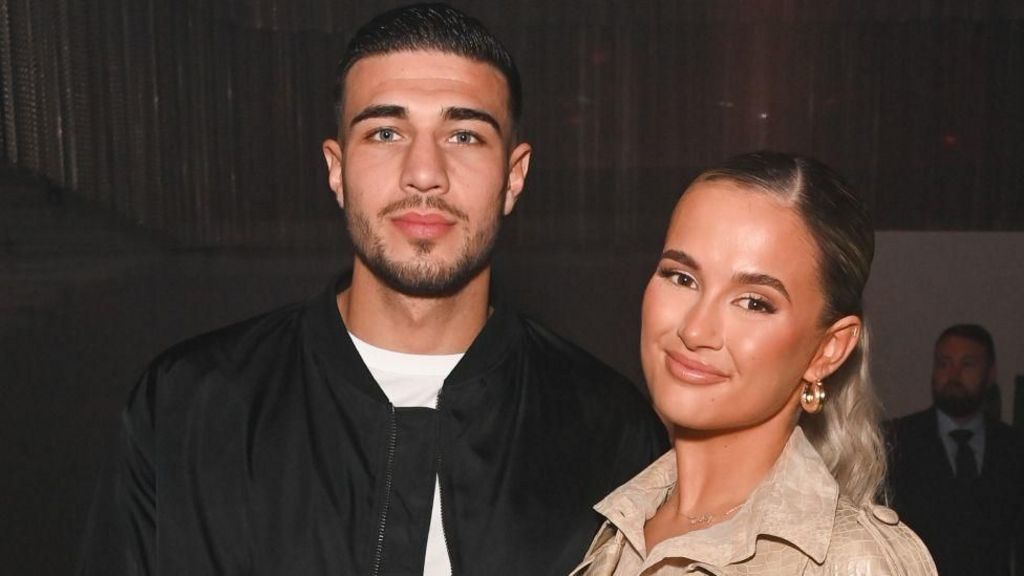 A picture of Tommy Fury wearing black, and Molly Mae in a light coloured top against a dark backdrop