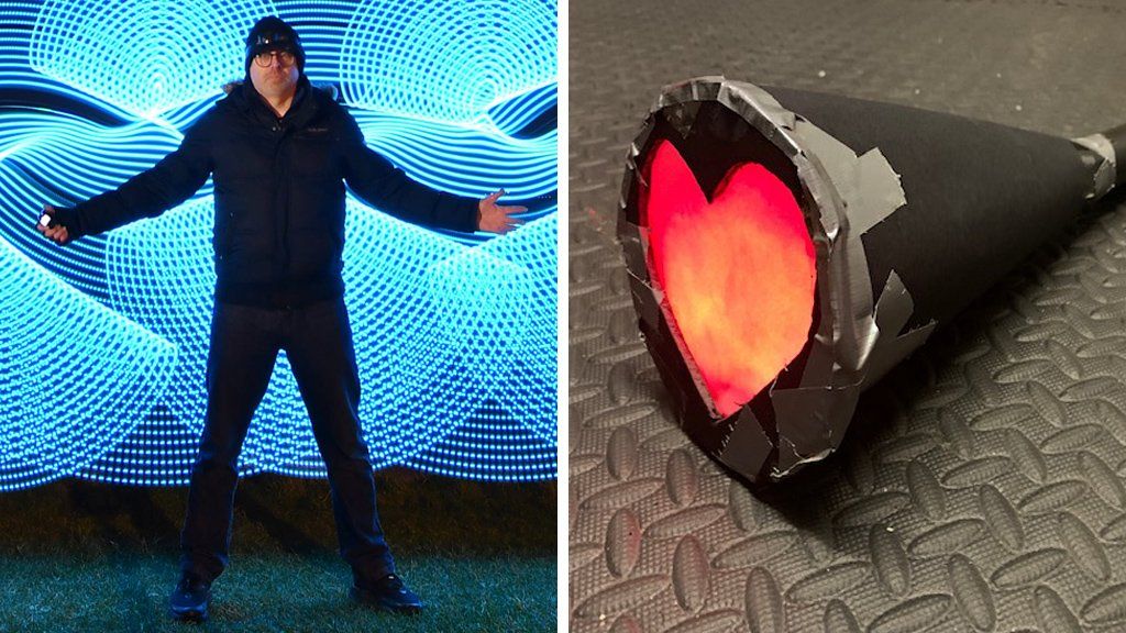 Light painter Kevin Jay standing against blue light patterns and a torch created in a heart shape that was used to create the heart light patterns