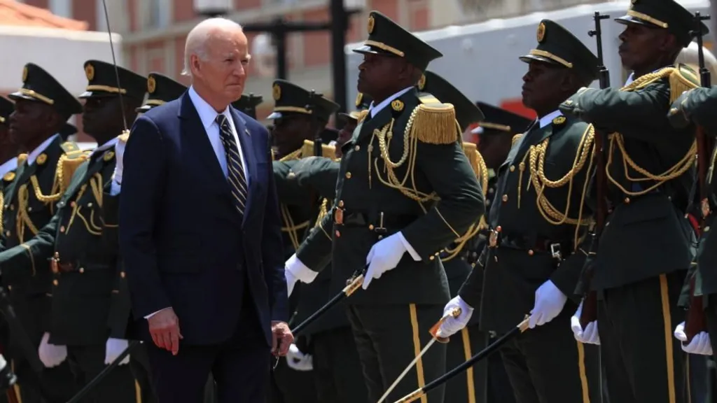 Joe Biden reviews a guard of honour as he arrives at the presidential palace in Luanda. He is walking past a group of soldiers in formal uniforms, wearing white gloves and holding swords.