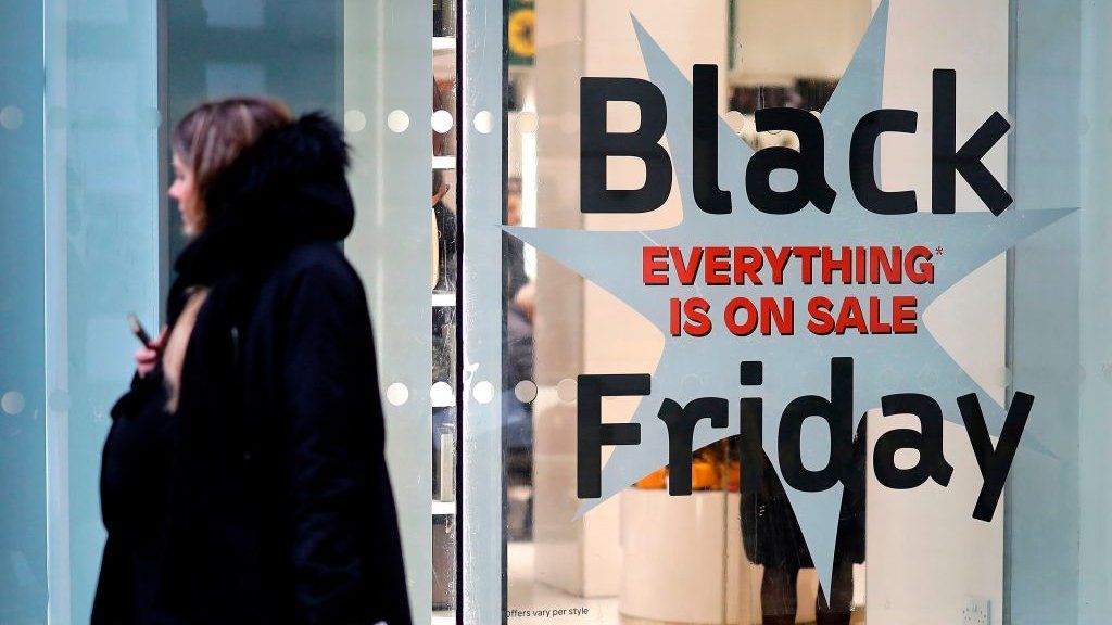 Shoppers pass a promotional sign for 'Black Friday' sales discounts, outside a store on Oxford Street in London, on November 26, 2019