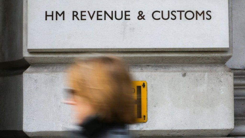 A woman walks in front of the HMRC building sign in Whitehall