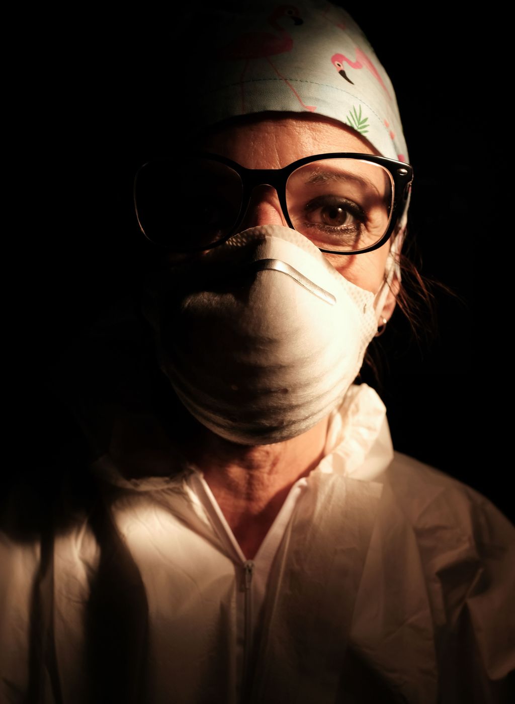 A female nurse wearing a face mask with a dark background behind her