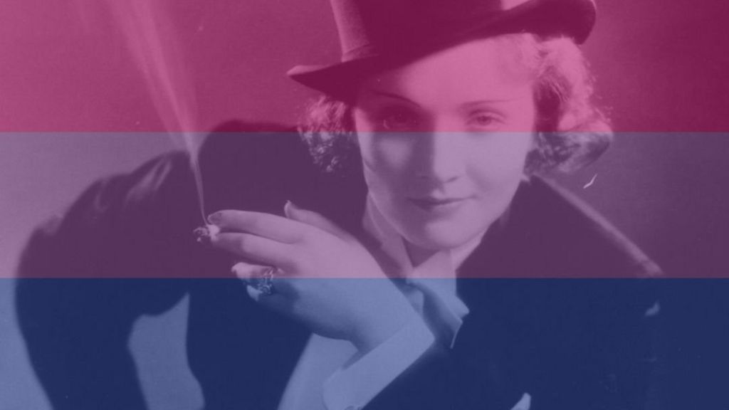 Marlene Dietrich looking to camera while dressed in a top hat and suit smoking a cigarette