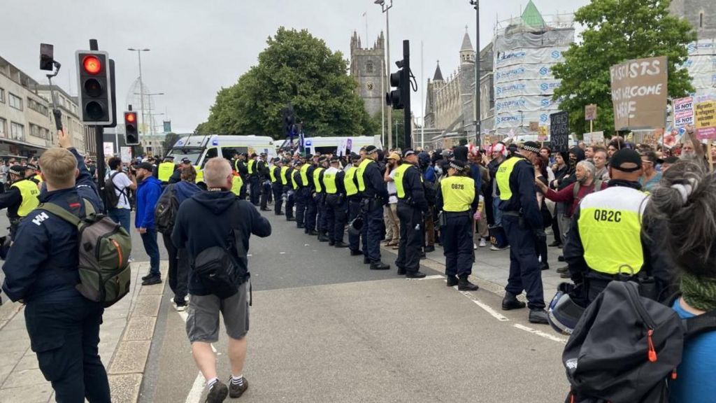 Plymouth city centre protest showing a line of riot police facing protesters