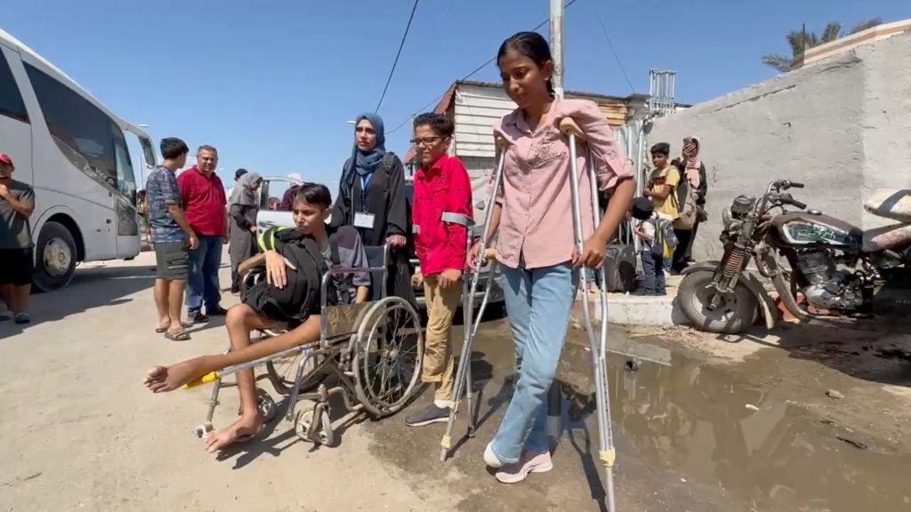 Sarah Marzouk, who is on crutches after losing her foot, waits with a group of people (30/07/24)