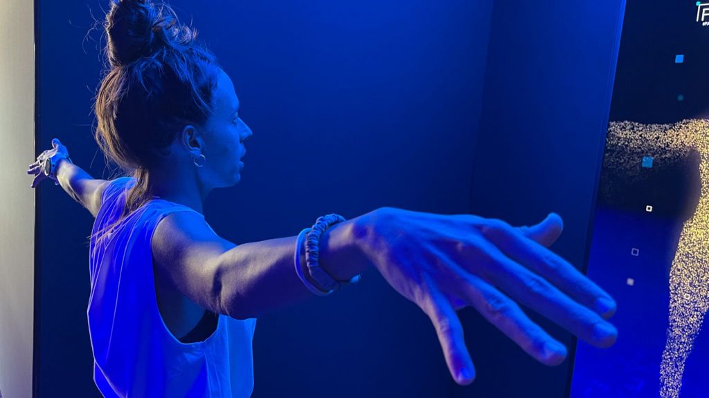 A woman stands with her arms out in front of a digital display